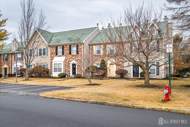 townhome / multi-family property with uncovered parking, brick siding, a front lawn, and a chimney