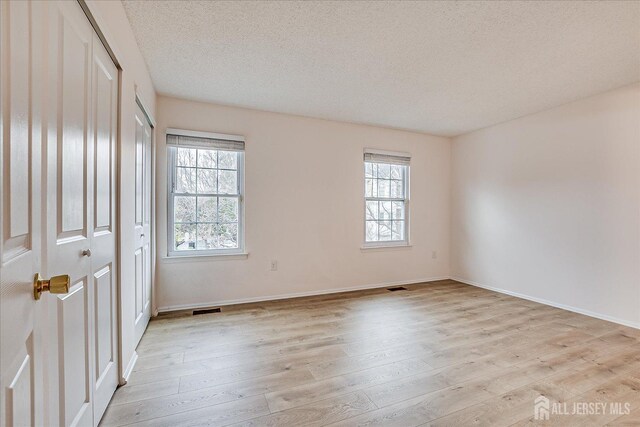 unfurnished room with baseboards, visible vents, light wood-style flooring, and a textured ceiling