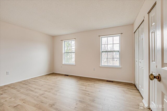 unfurnished bedroom with a textured ceiling, light wood-type flooring, visible vents, and baseboards