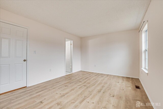 unfurnished room featuring baseboards, a textured ceiling, visible vents, and wood finished floors