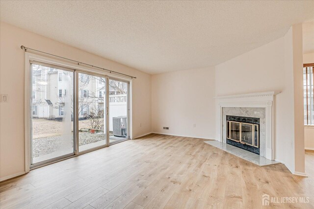 unfurnished living room with wood finished floors, a high end fireplace, and a healthy amount of sunlight