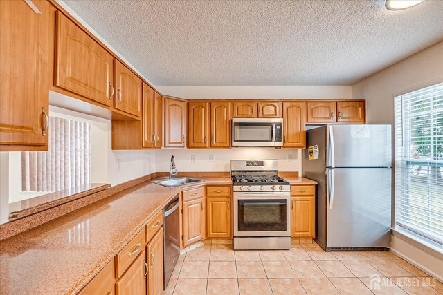 kitchen with brown cabinets, light tile patterned floors, stainless steel appliances, and a sink