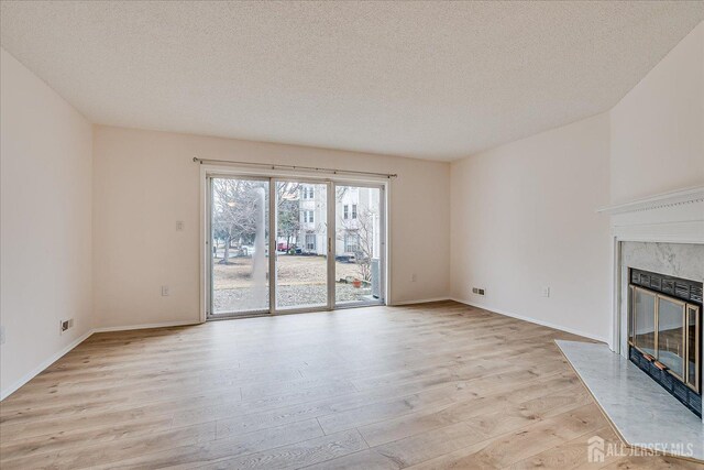 unfurnished living room with a high end fireplace, baseboards, a textured ceiling, and light wood finished floors