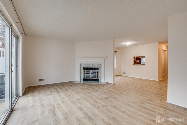 unfurnished living room featuring light wood-style floors, a premium fireplace, visible vents, and a textured ceiling