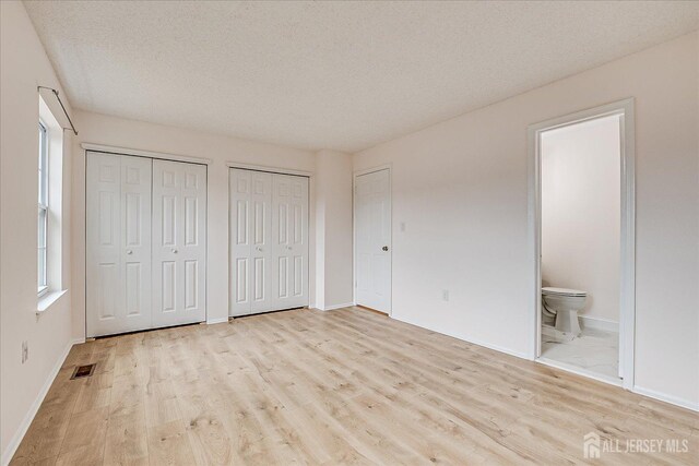 unfurnished bedroom featuring a textured ceiling, wood finished floors, visible vents, and multiple closets