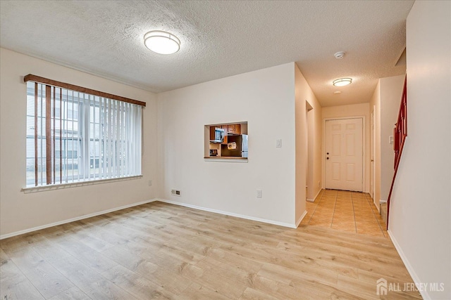 spare room with light wood-style flooring, baseboards, and a textured ceiling