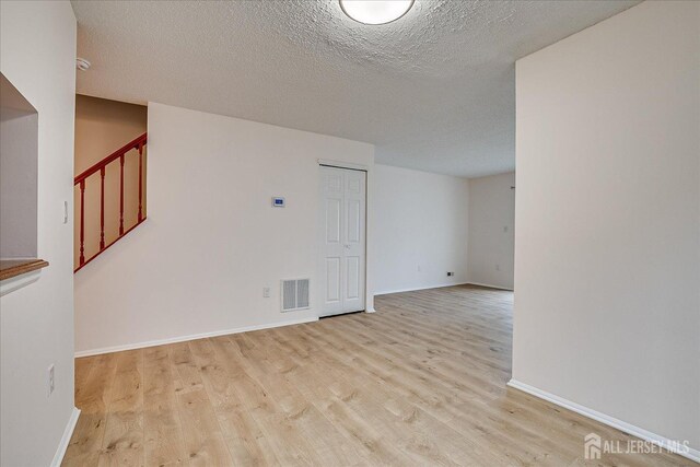 spare room featuring visible vents, stairway, a textured ceiling, wood finished floors, and baseboards