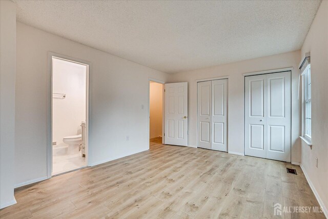 unfurnished bedroom featuring a textured ceiling, wood finished floors, visible vents, multiple closets, and ensuite bath