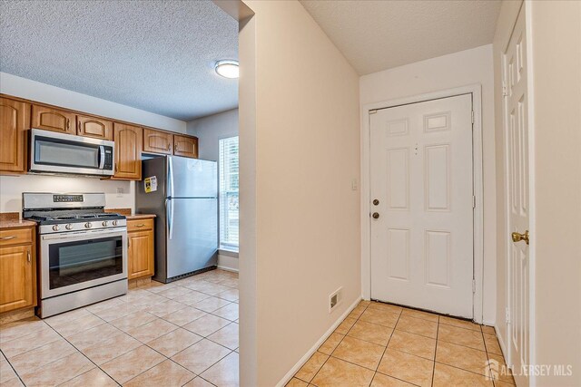 kitchen featuring light tile patterned floors, visible vents, appliances with stainless steel finishes, and brown cabinets