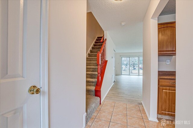 hall featuring a textured ceiling, light tile patterned flooring, stairs, and baseboards