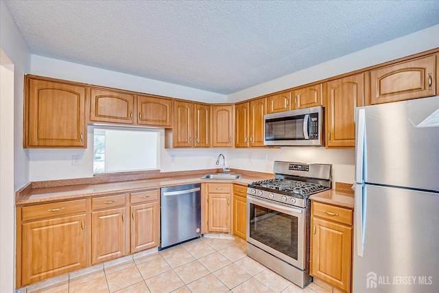 kitchen with a textured ceiling, light tile patterned flooring, a sink, light countertops, and appliances with stainless steel finishes