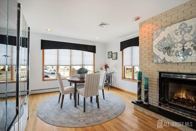 dining space with a brick fireplace, light wood-style flooring, visible vents, and ornamental molding