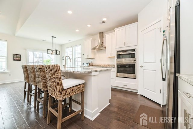 20 Metro Dr, Monroe, NJ 08831 - kitchen featuring wall chimney range hood, stainless steel appliances, dark wood-type flooring, white cabinetry, and light stone counters