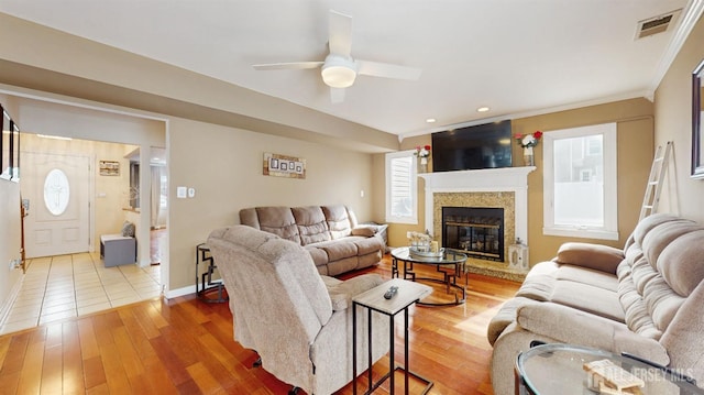 living area featuring hardwood / wood-style flooring, a ceiling fan, visible vents, baseboards, and a glass covered fireplace