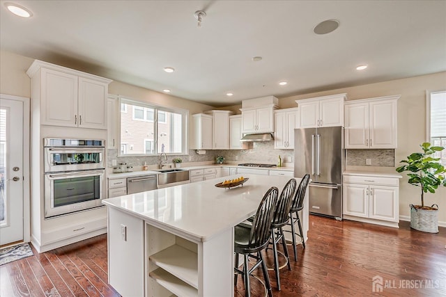 kitchen with sink, appliances with stainless steel finishes, white cabinets, a kitchen island, and dark hardwood / wood-style flooring