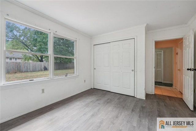 unfurnished bedroom featuring baseboards, a closet, wood finished floors, and crown molding