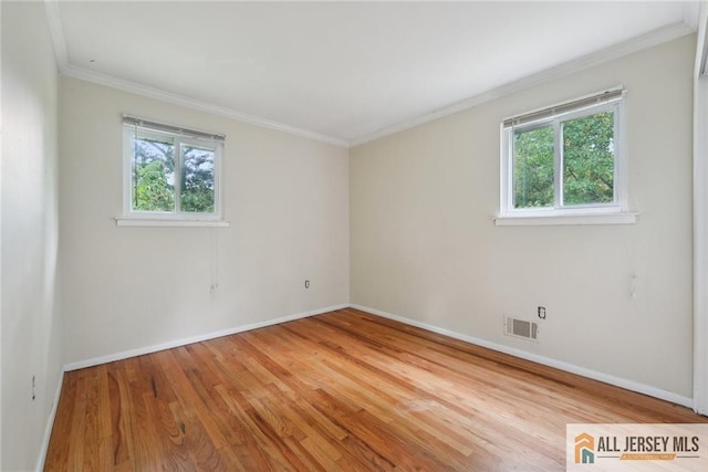 empty room with baseboards, wood finished floors, visible vents, and crown molding