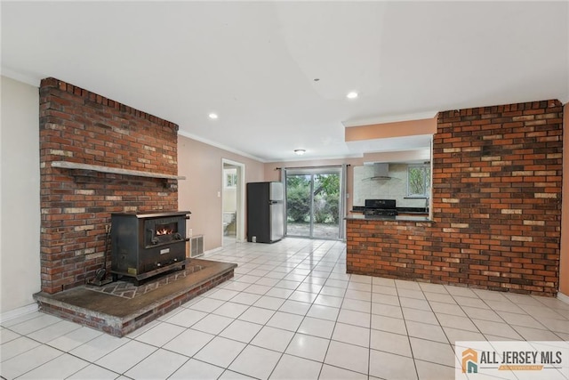 unfurnished living room with light tile patterned flooring, visible vents, baseboards, a wood stove, and crown molding