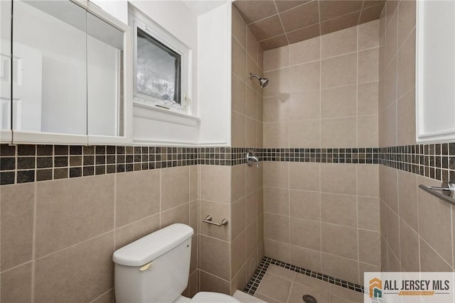 bathroom featuring toilet, a wainscoted wall, tile walls, and tiled shower