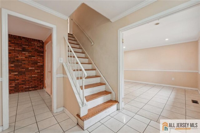 stairway featuring tile patterned flooring, brick wall, and ornamental molding