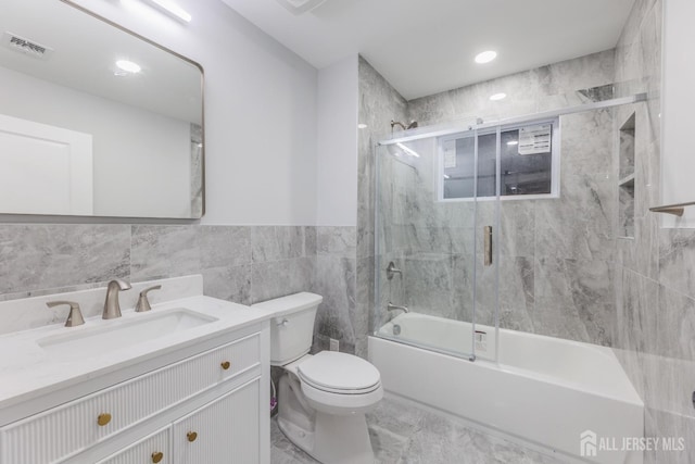 full bathroom with tile walls, visible vents, toilet, combined bath / shower with glass door, and vanity