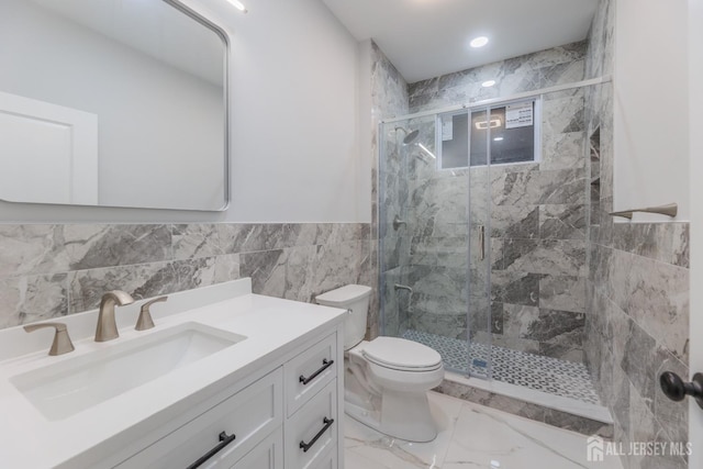 full bath with a stall shower, toilet, marble finish floor, vanity, and tile walls