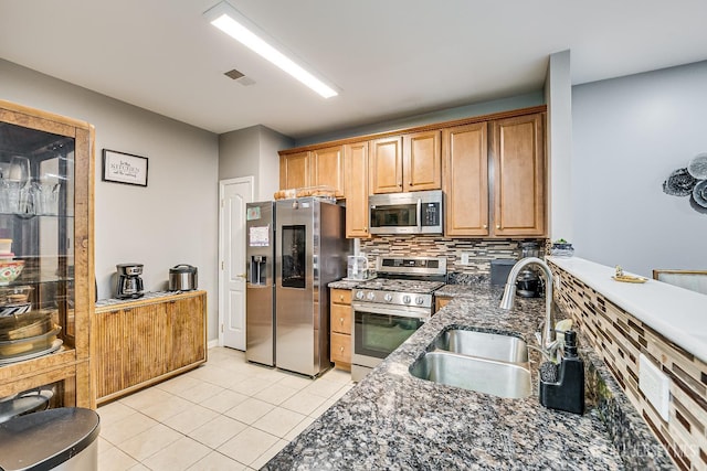 kitchen with sink, light tile patterned floors, appliances with stainless steel finishes, dark stone countertops, and backsplash