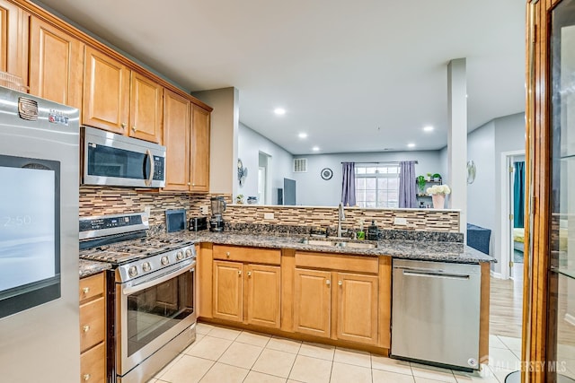 kitchen featuring sink, light tile patterned floors, stainless steel appliances, decorative backsplash, and dark stone counters