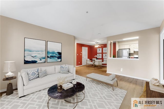 living area with baseboards, a ceiling fan, and light wood-style floors