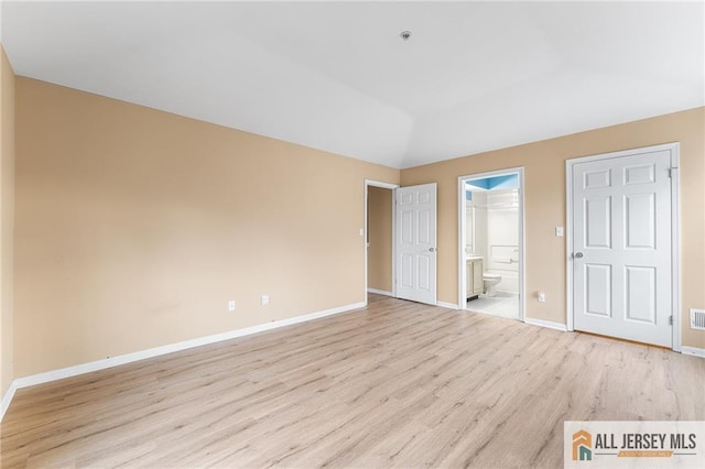 unfurnished bedroom featuring lofted ceiling, light wood finished floors, ensuite bathroom, and baseboards