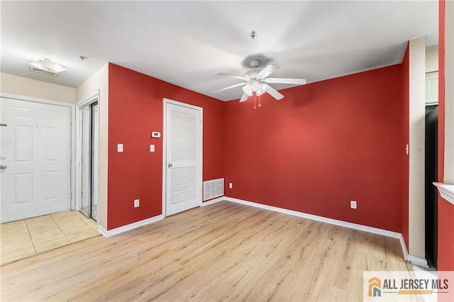 empty room featuring light wood-style floors, ceiling fan, visible vents, and baseboards