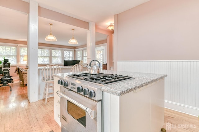 kitchen with light wood finished floors, high end range, wainscoting, and light stone countertops