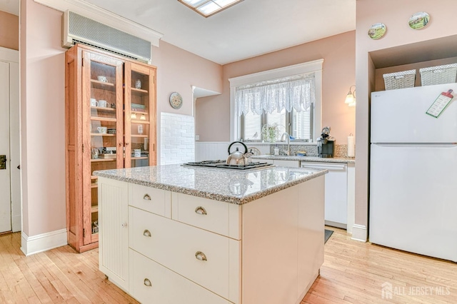 kitchen with a center island, a sink, white appliances, light wood finished floors, and light stone countertops