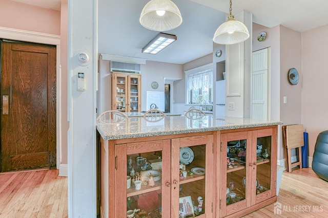 kitchen featuring light stone countertops, light wood finished floors, freestanding refrigerator, and a wall unit AC