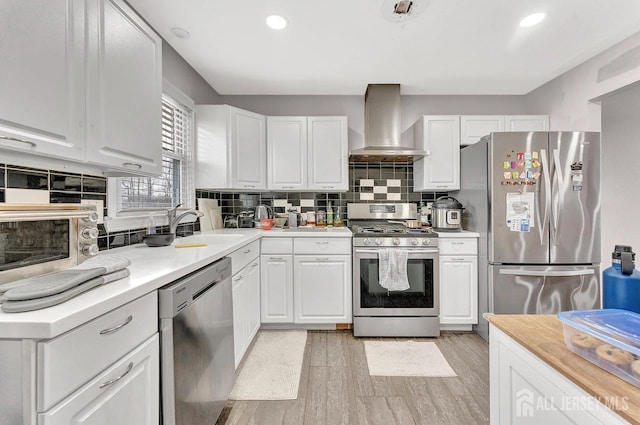 kitchen with stainless steel appliances, white cabinetry, wall chimney range hood, and tasteful backsplash