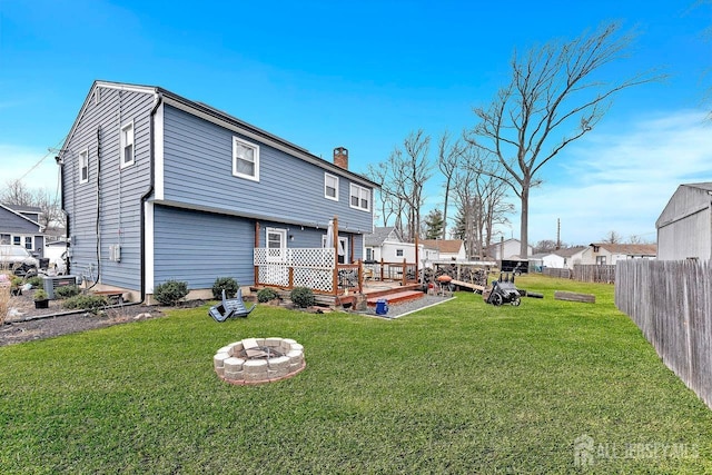 back of property with a fire pit, fence, a lawn, a wooden deck, and a chimney