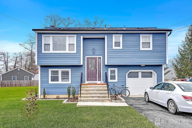 raised ranch with an attached garage, aphalt driveway, and a front yard