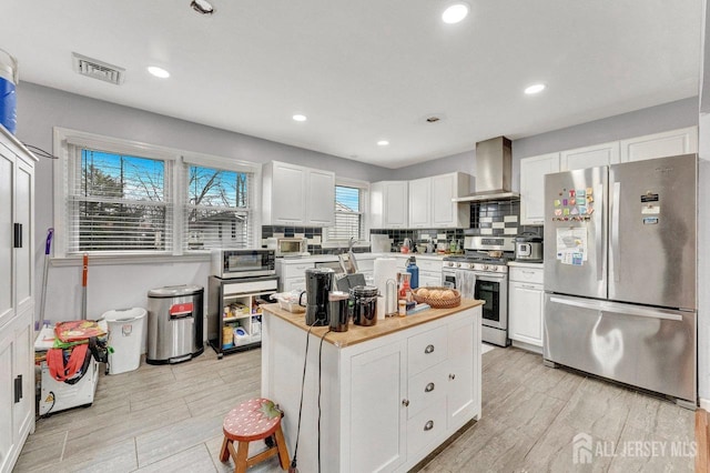 kitchen featuring appliances with stainless steel finishes, visible vents, wall chimney range hood, and decorative backsplash