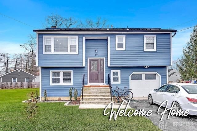 bi-level home with an attached garage, driveway, fence, and a front yard