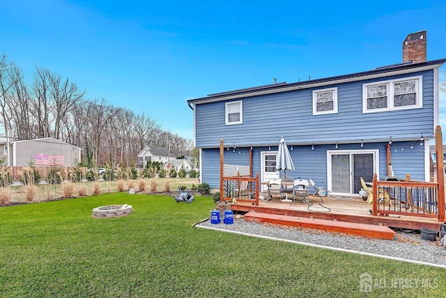 back of house with an outdoor fire pit, a chimney, a wooden deck, and a yard