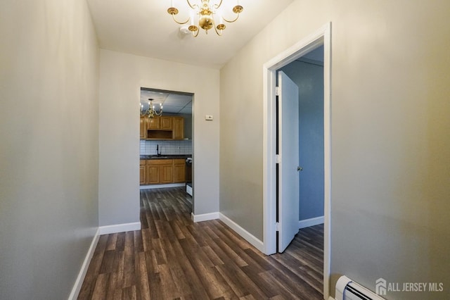 hall featuring a chandelier, a baseboard heating unit, dark wood finished floors, and baseboards