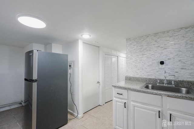 kitchen with light tile patterned floors, tasteful backsplash, freestanding refrigerator, white cabinetry, and a sink