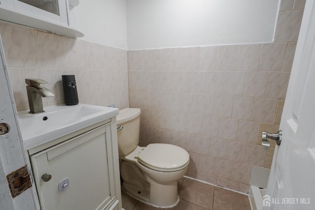 half bathroom with toilet, tile patterned flooring, tile walls, and vanity