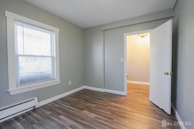 spare room featuring baseboards, a baseboard heating unit, and wood finished floors