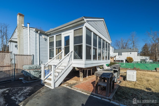 rear view of property featuring a chimney, a patio area, fence, and a sunroom