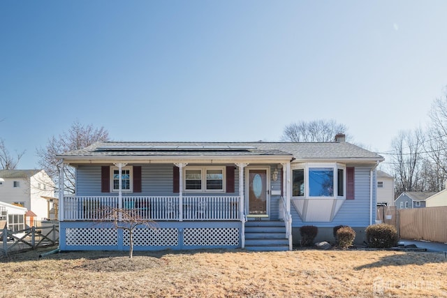 view of front of house featuring covered porch, roof with shingles, fence, and roof mounted solar panels