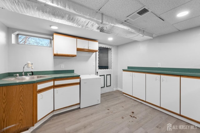 kitchen with visible vents, light wood finished floors, refrigerator, a sink, and white cabinetry