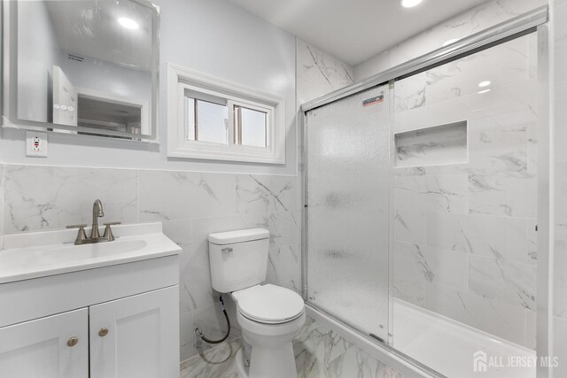 bathroom featuring vanity, toilet, a shower with door, and tile walls