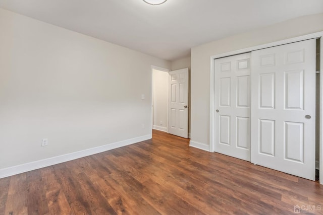 unfurnished bedroom featuring a closet, baseboards, and dark wood-style flooring