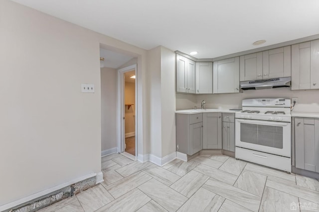 kitchen featuring gas range gas stove, under cabinet range hood, light countertops, gray cabinets, and a sink